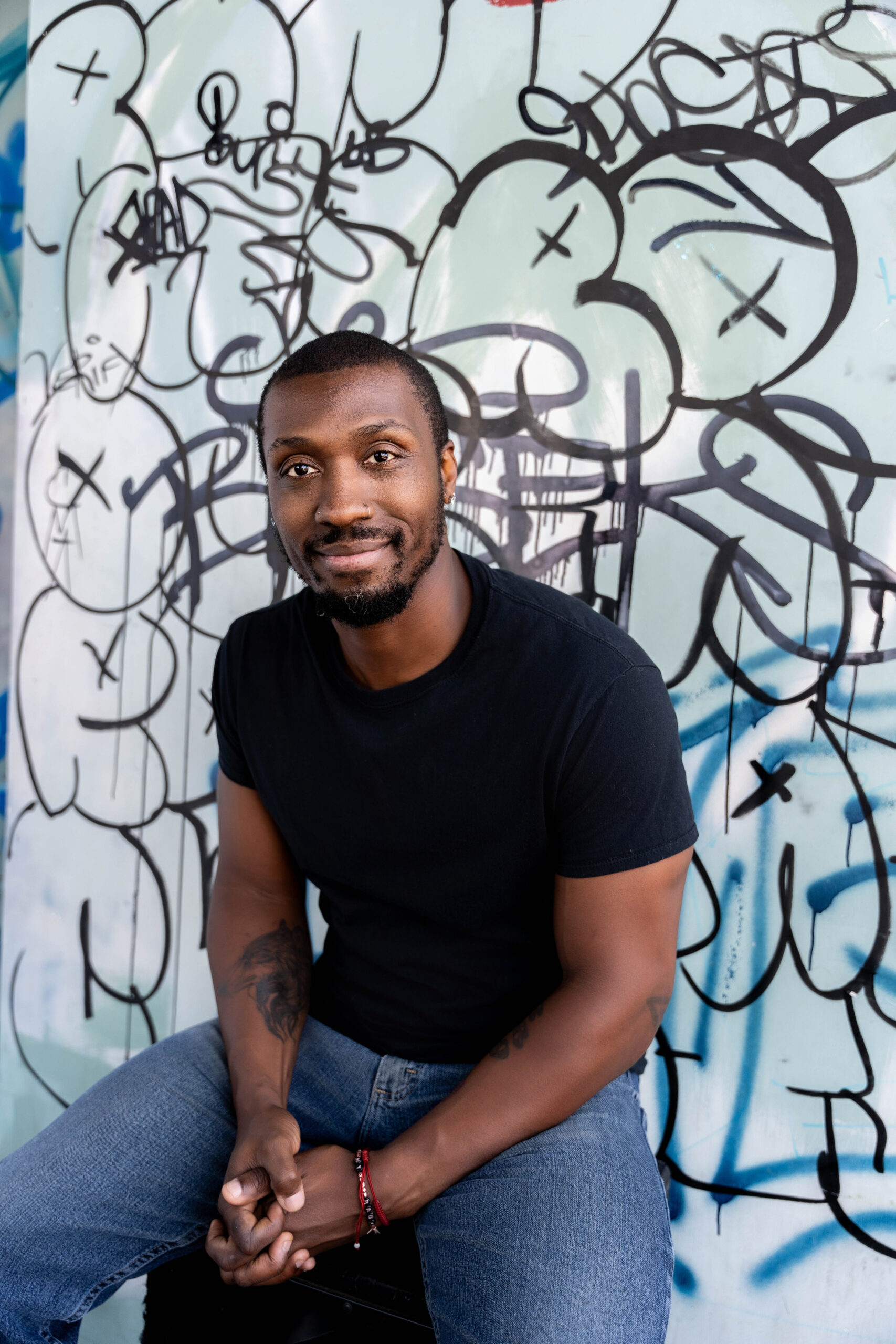 A man in a black shirt and jeans sits against a graffiti covered wall inside a club