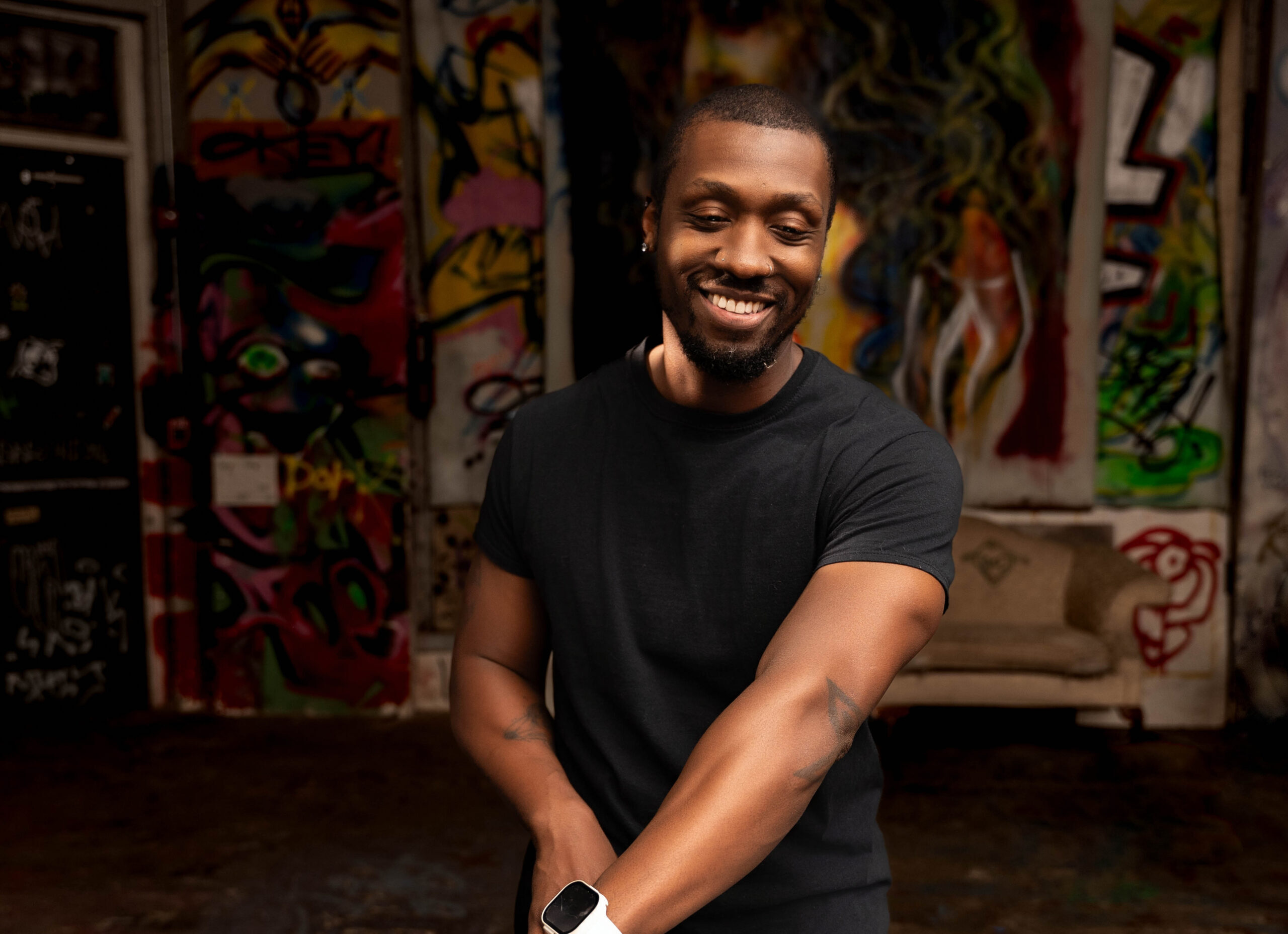 A DJ in a black shirt smiles while working his system in a graffiti covered room during Personal Brand Photos For Business