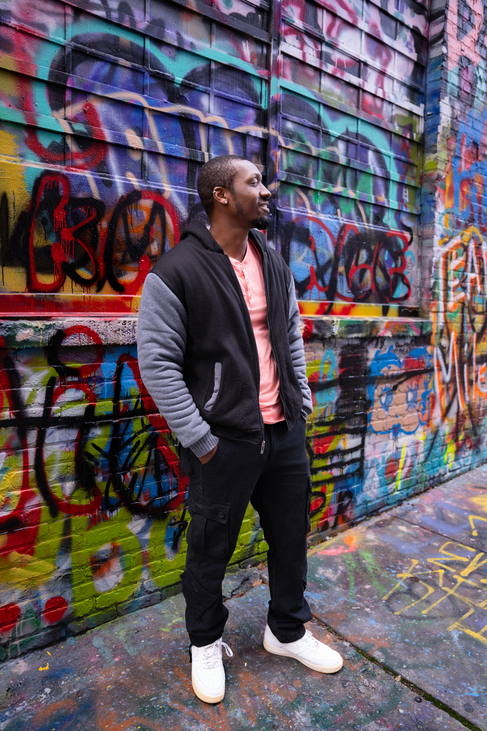 A DJ stands in an alley against a graffiti wall in a black jacket during Personal Brand Photos For Business