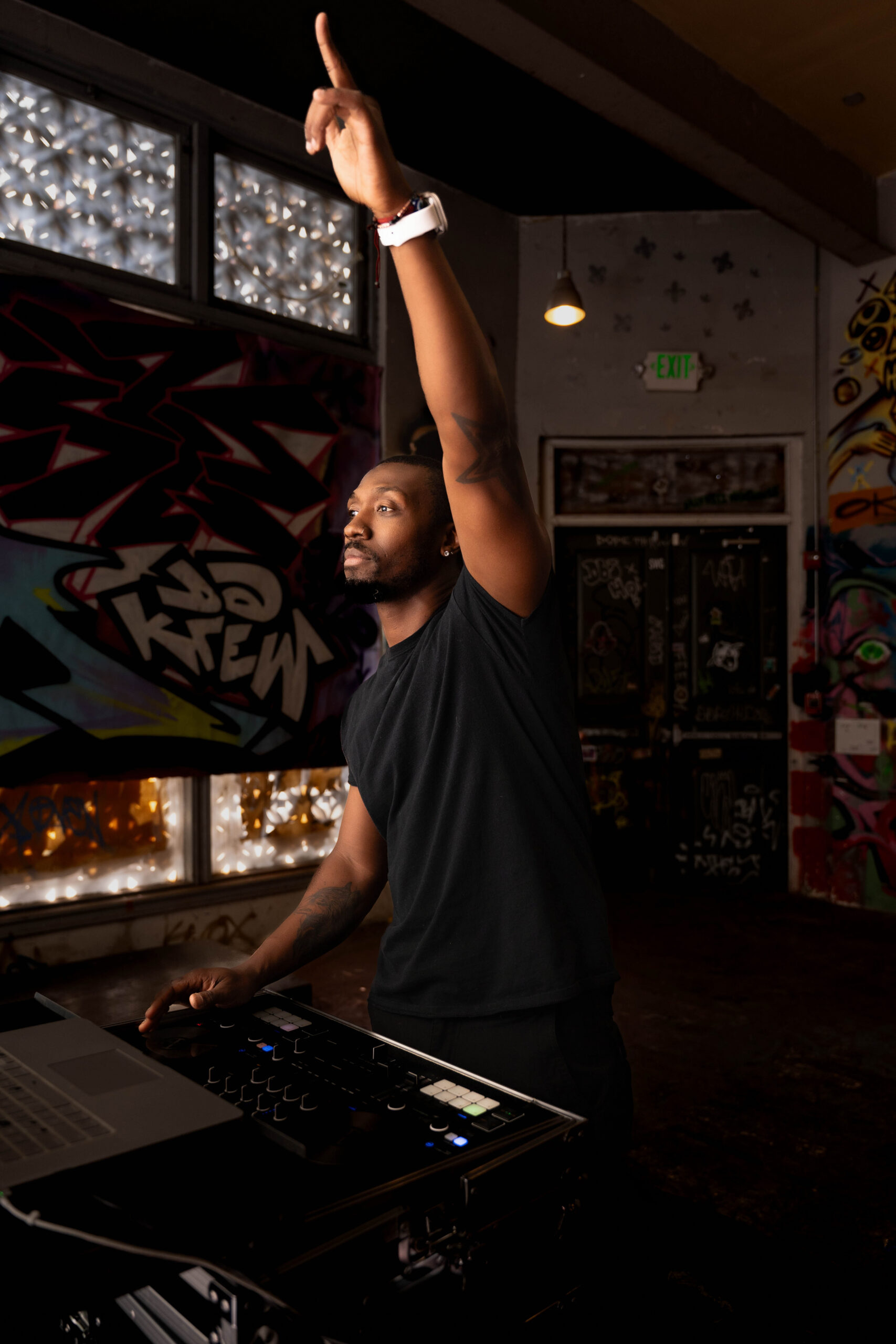 A DJ raises a hand while working in a graffiti covered club