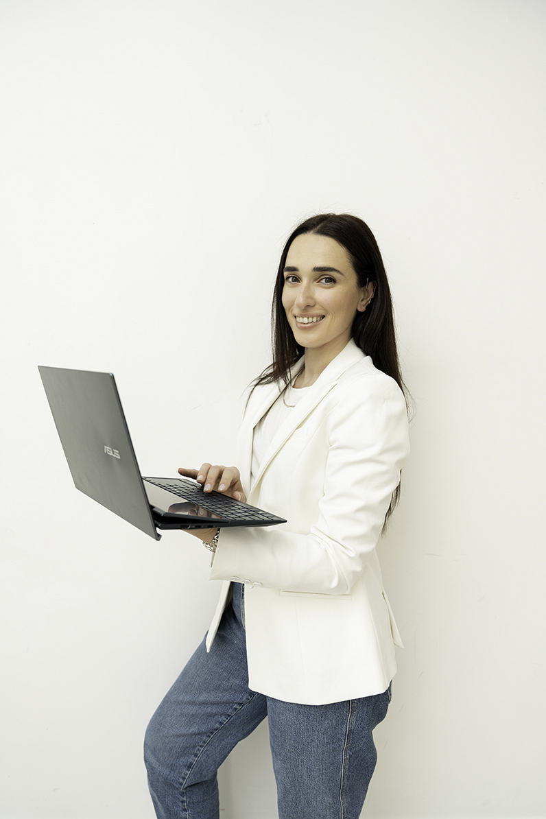 A woman stands in a studio working on her laptop in jeans and a white blazer for Baltimore Personal Brand Photos