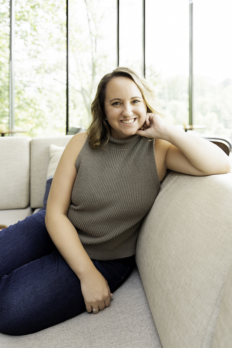 A woman sits on a couch smiling in a grey blouse and jeans during a DC personal branding session