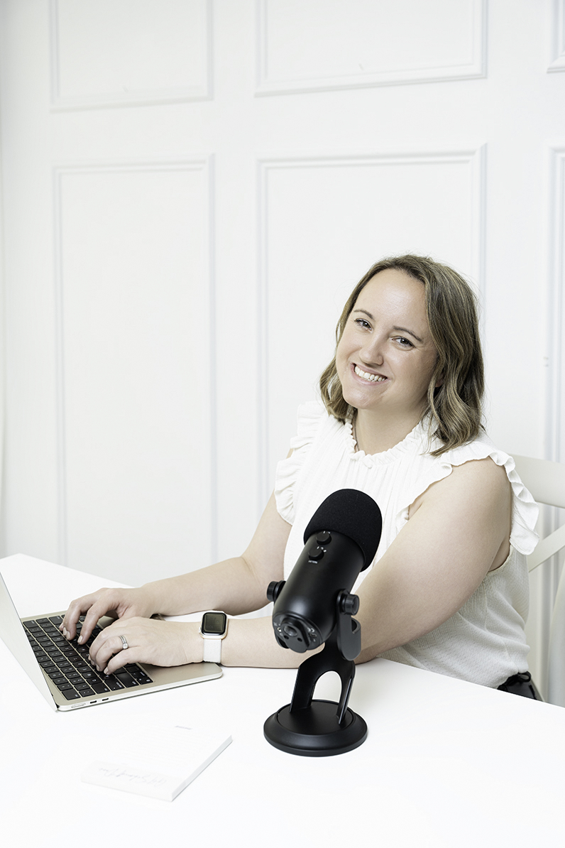 A happy woman works on her laptop with a microphone in a white room