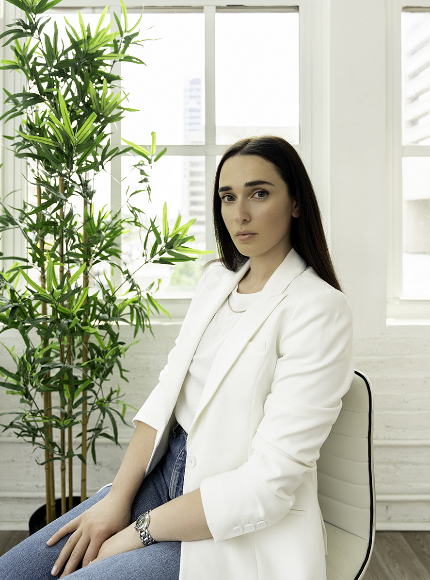 A woman stares while sitting in a modern office chair in a studio in a white blouse