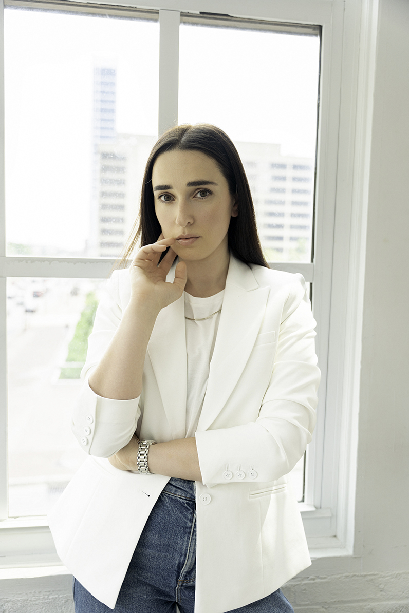 A woman rests finger on her chin while standing in a window in a white blouse to Invest in Personal Branding Photos