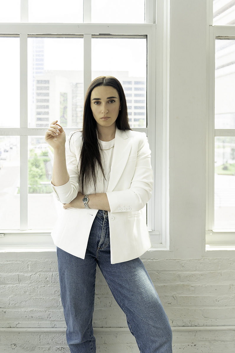 A woman stands in a window wearing a white blouse and jeans after learning to Invest in Personal Branding Photos