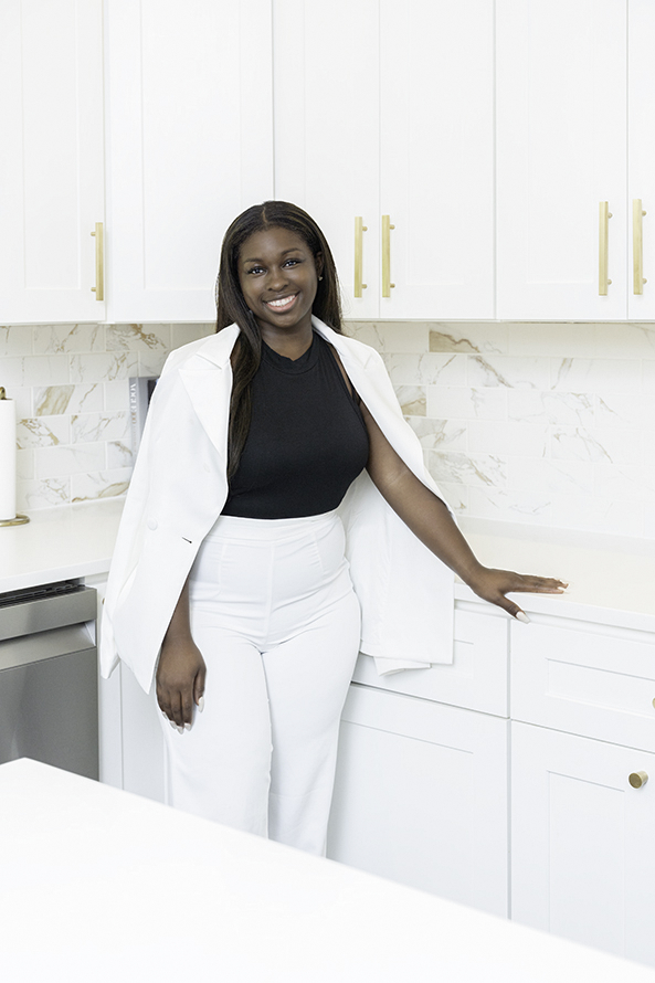 A woman in a white blazer leans on a kitchen counter smiling during Personal Branding Photos Maryland