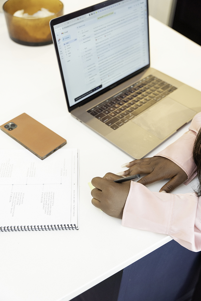 Details of a woman holding a pen while working on her laptop at a white desk during her Personal Branding Session