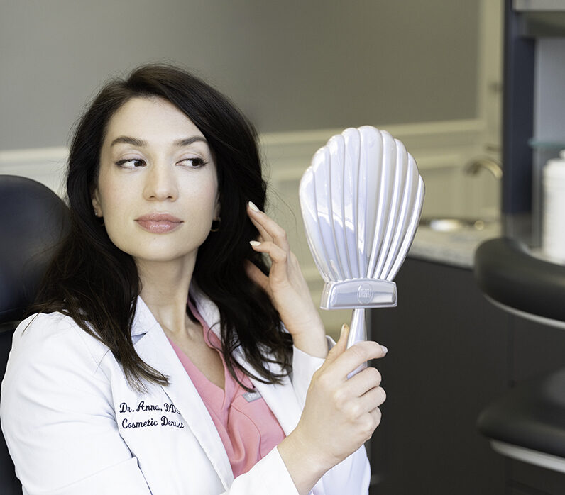 A doctor in pink scrubs sits back in a chair looking in a mirror