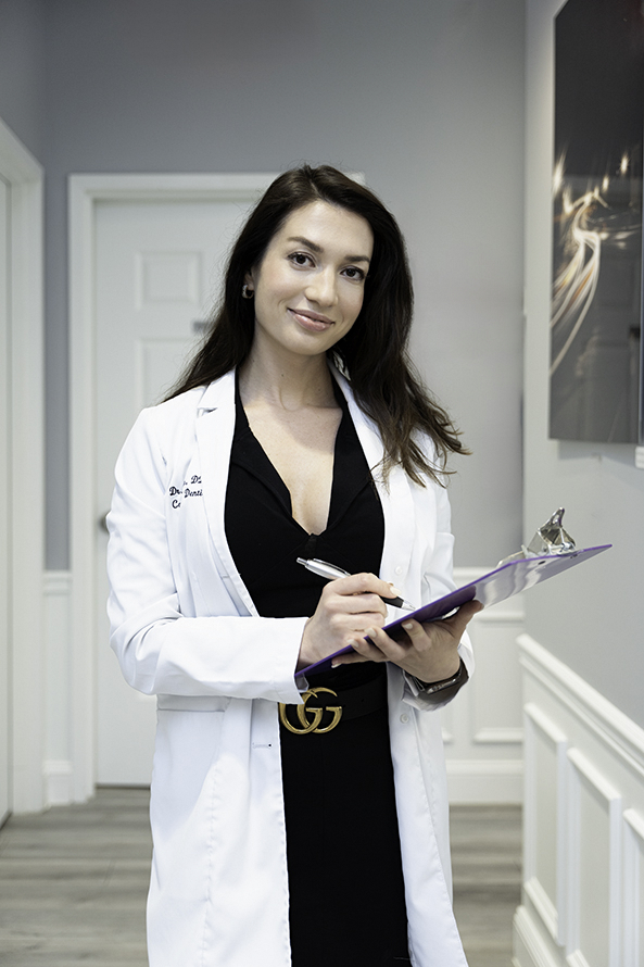 A doctor walks in a hallway writing on a clipboard in a black dress