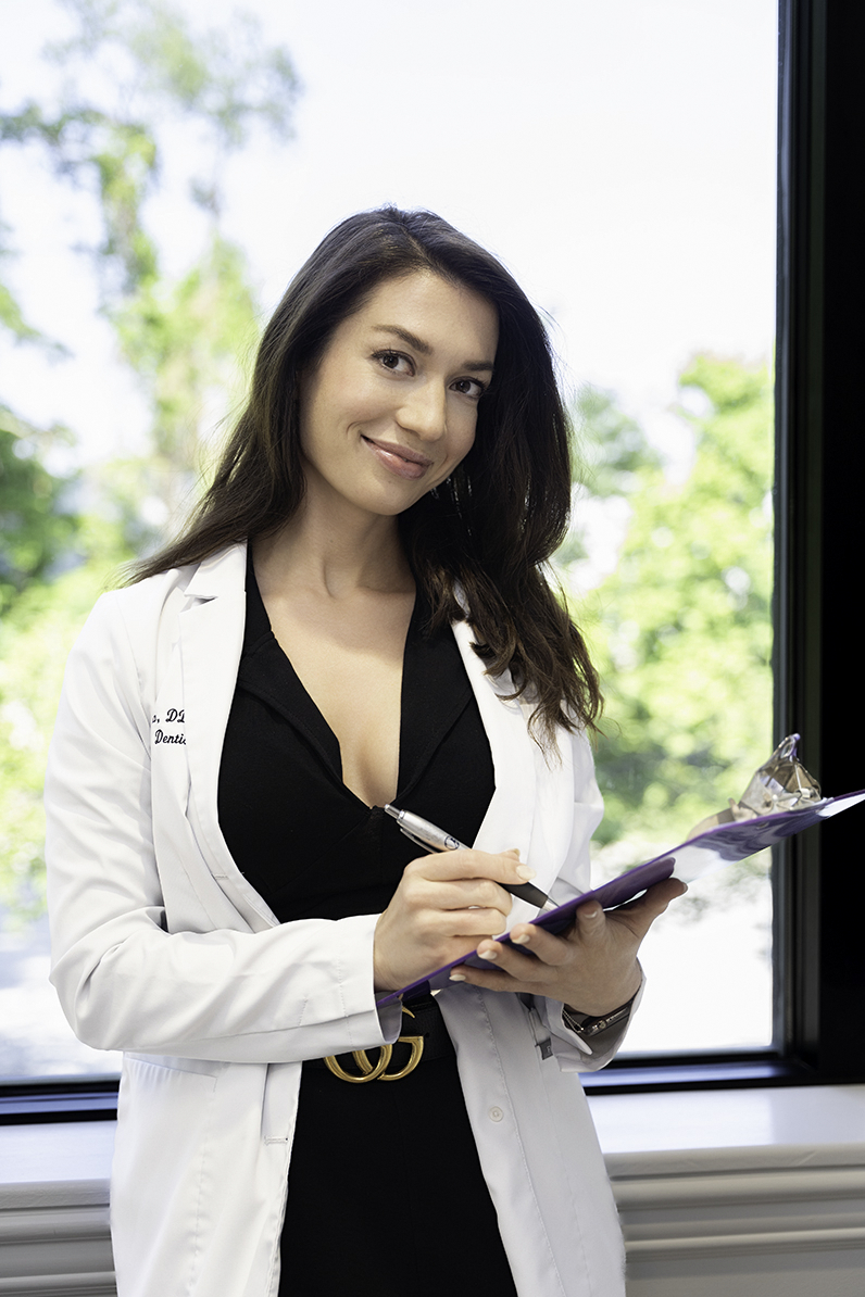 A woman doctor in a black dress writes on a clipboard while smiling in a window after finding ways to use personal branding photos