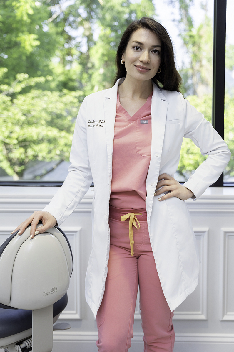 A doctor in pink scrubs stands in an office window leaning on a rolling chair with a hand on her hip after finding ways to use personal branding photos